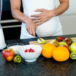 Pregnant woman touching her belly while cutting fruits