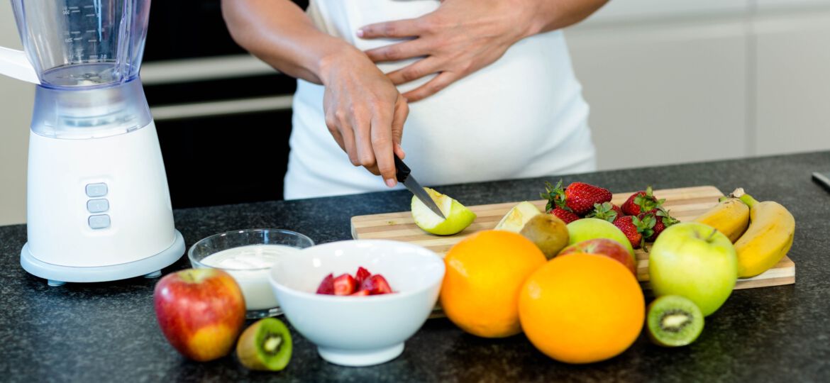 Pregnant woman touching her belly while cutting fruits